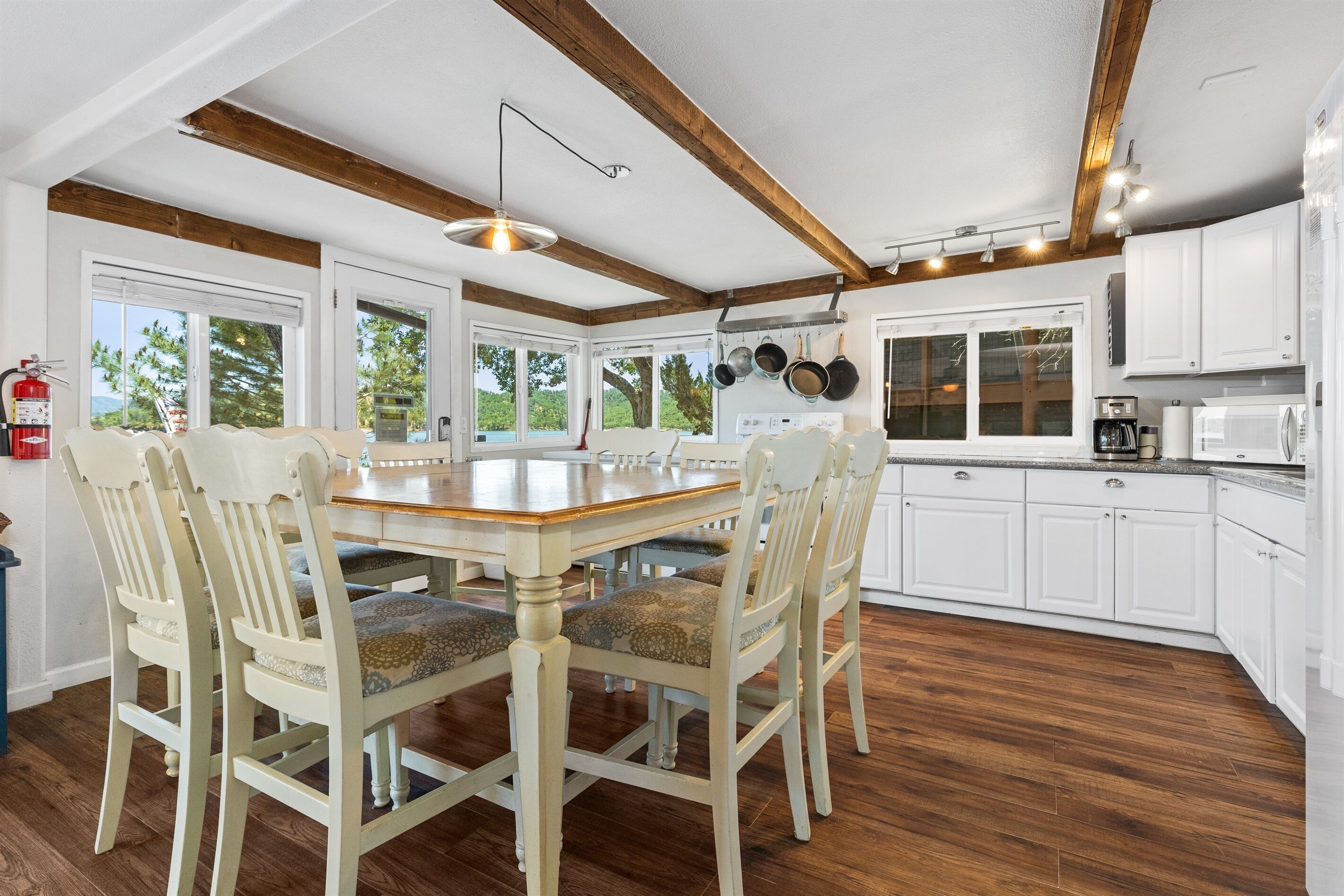 Une cuisine spacieuse avec des poutres en bois, des armoires blanches et une grande table à manger entourée de chaises.