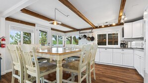 A spacious kitchen with wooden beams, white cabinets, and a large dining table with chairs.