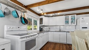 A modern kitchen with white cabinetry, a built-in oven, and a microwave. There are hanging pots and a white refrigerator.