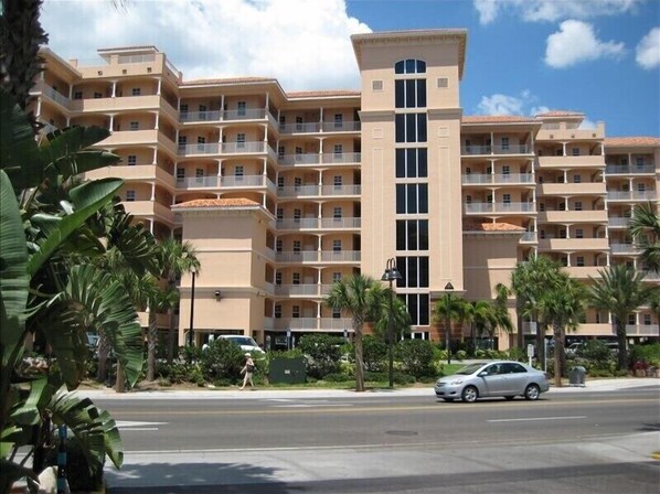 Un hotel de varios pisos con balcones, una torre central y palmeras al frente.