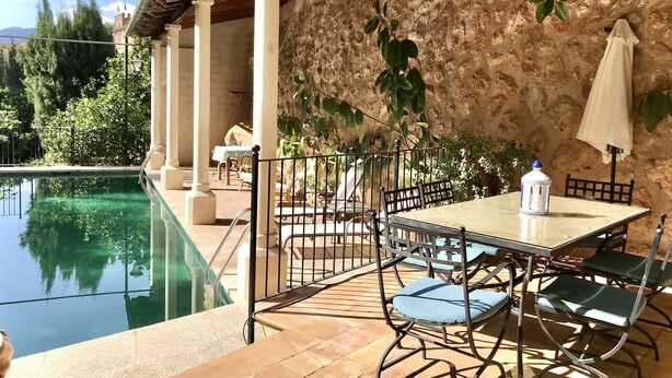 A poolside area with a table and chairs, a pergola, and a stone wall. - Stunning Villa and Garden w/ Pool and Sweeping Views in the Heart of Fornalutx (Fornalutx)