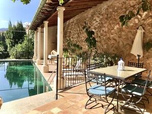 Ein Poolbereich mit Tisch und Stühlen, einer Pergola und einer Steinmauer.