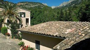 A stone building with a tiled roof, surrounded by lush greenery and mountains. - Stunning Villa and Garden w/ Pool and Sweeping Views in the Heart of Fornalutx (Fornalutx)