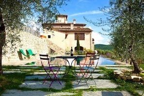 A stone house with a swimming pool, outdoor seating, and a stone wall.