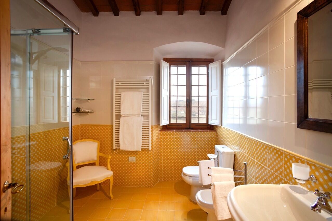 A bathroom with a glass shower enclosure, a toilet, a sink, and a chair.