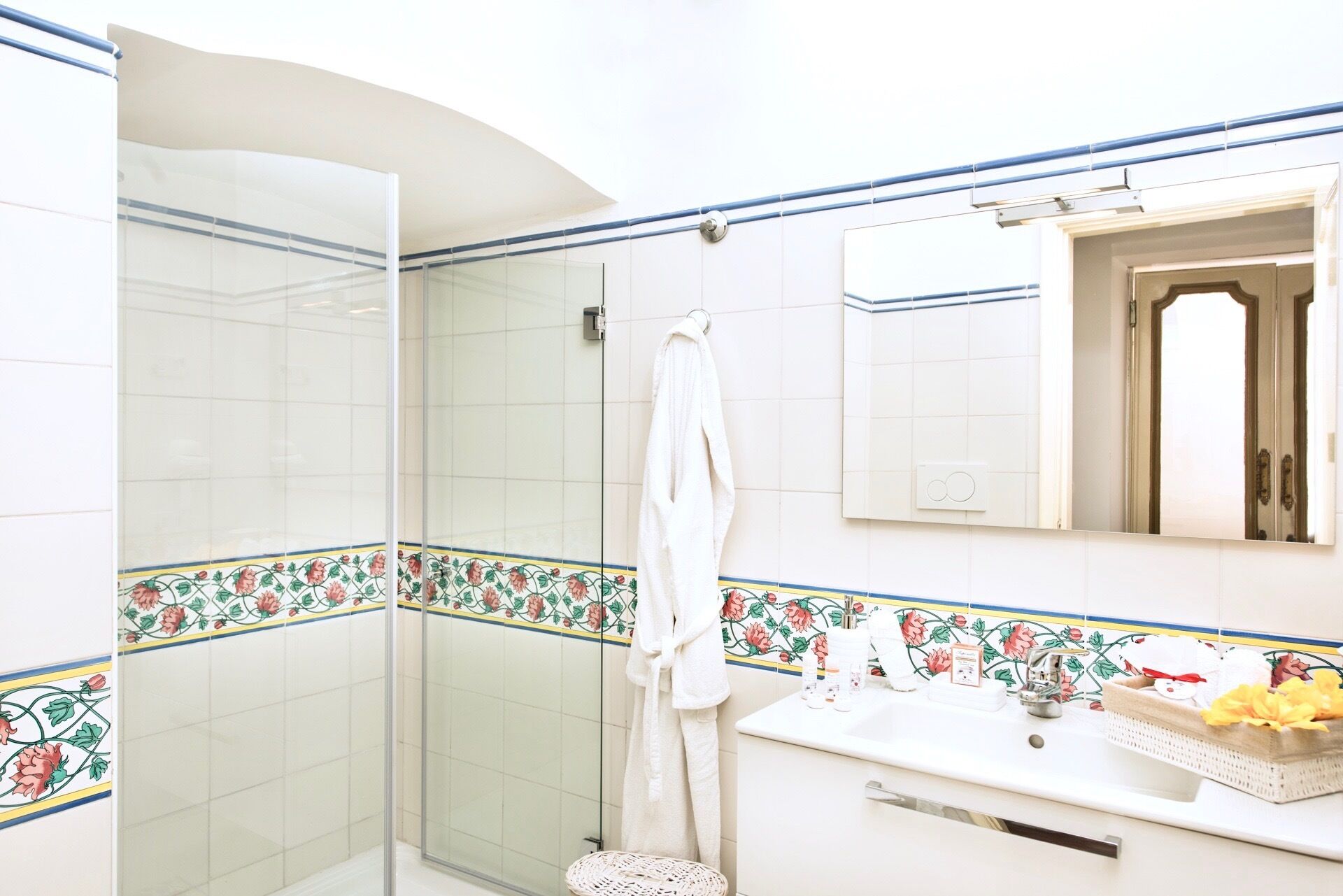 A bathroom with a glass shower enclosure, a white sink with toiletries, and a mirror above the sink.