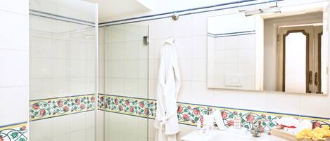 A bathroom with a glass shower enclosure, a white sink with toiletries, and a mirror above the sink.
