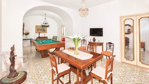 Una habitación con mesa de billar, mesa de comedor con sillas, candelabro y televisor.
