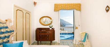 Une chambre d’hôtel avec un lit, une commode, un miroir, un balcon donnant sur une piscine et une vue sur la mer.