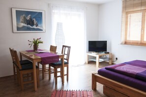 A room with a bed, a desk with a TV, a dining table with chairs, and a painting on the wall.