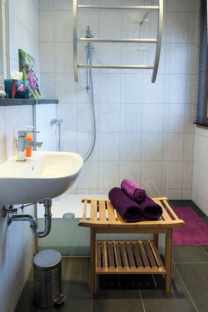 A bathroom with a sink, shower, and a wooden bench with towels.