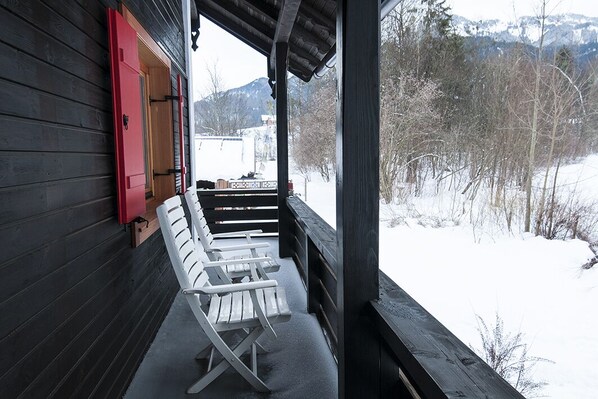 A wooden cabin with a porch, white Adirondack chairs, and a red door.