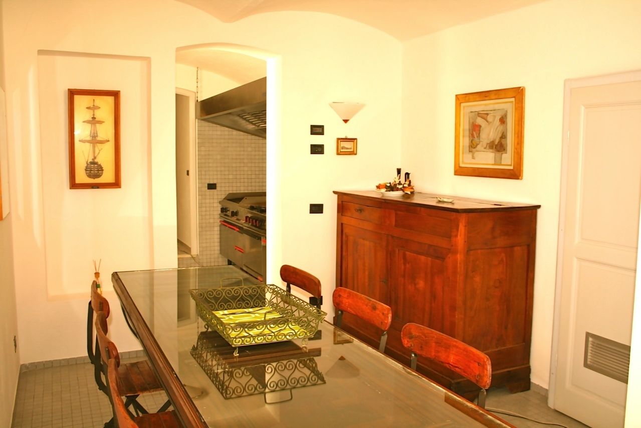A dining area with a glass table, wooden chairs, a wooden cabinet, and framed artwork on the walls.