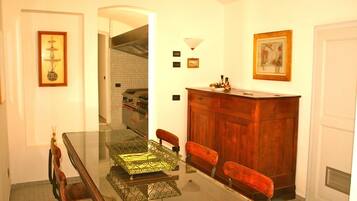 A dining area with a glass table, wooden chairs, a wooden cabinet, and framed artwork on the walls.