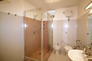Uma casa de banho com chuveiro em cabine de vidro, bidé, sanita e lavatório com espelho.