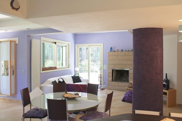 A modern living room with a fireplace, a round dining table, and a sofa. - Villa Stella Marina (Castiglione della Pescaia)