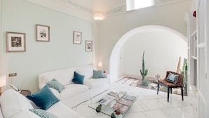 A spacious living room with a white sofa, a glass coffee table, and a cactus plant. - Villa Luce (Praiano)