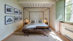 A bedroom with a four-poster bed, framed photographs on the wall, and a window with curtains. - Antico Brunello (Montalcino)