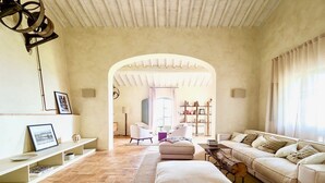 A spacious living room with a large sofa, a coffee table, and a fireplace. There is a bookshelf and a dining table in the background. - Antico Brunello (Montalcino)
