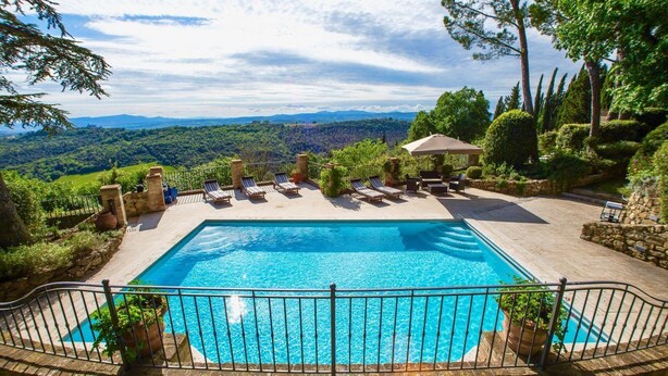 A rectangular pool with a surrounding deck, lounge chairs, and a stone wall. - Antico Brunello (Montalcino)