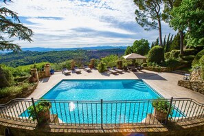 A rectangular pool with a surrounding deck, lounge chairs, and a stone wall. - Antico Brunello (Montalcino)
