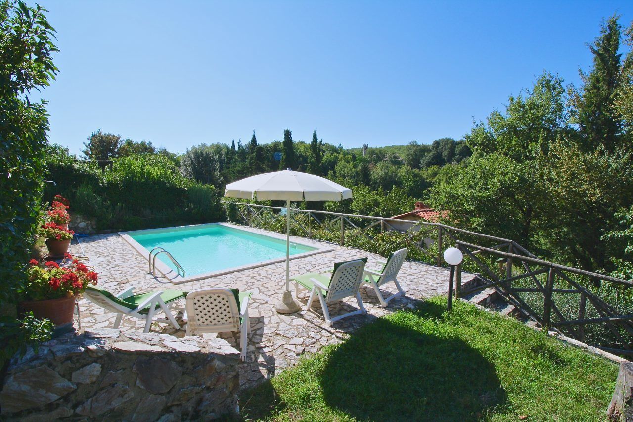A swimming pool with lounge chairs and an umbrella, surrounded by greenery and stone flooring.