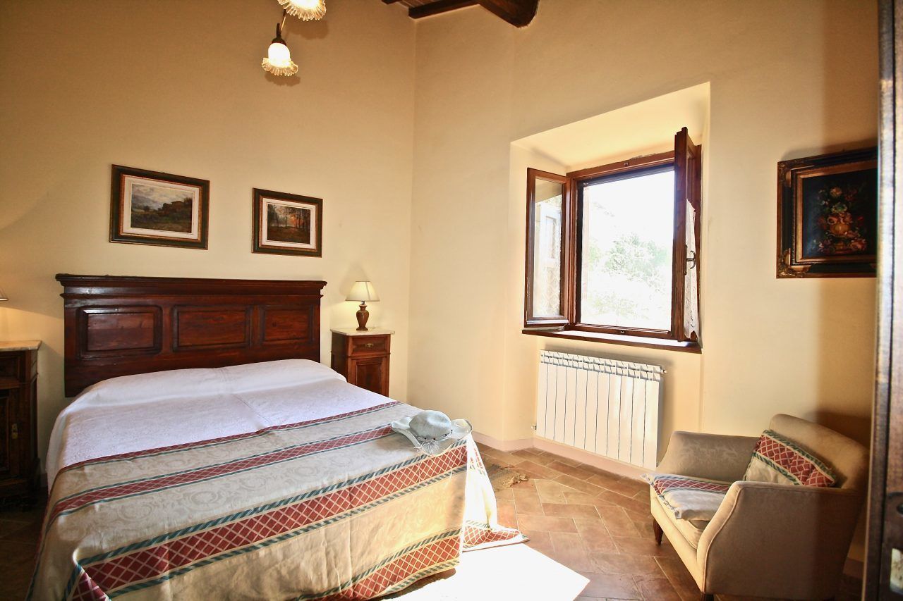 A bedroom with a large bed, a window, a chair, and framed pictures on the wall.