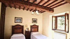 Quarto com duas camas de madeira, uma mesa pequena com abajur e uma janela com cortinas.