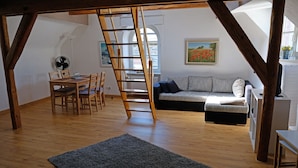 A loft-style room with a wooden floor, a dining table with chairs, a sofa, a ladder, and a fan. - Haus Weihertor (Traben-Trarbach)