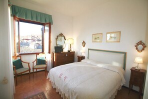 Un dormitorio con una cama grande, un aparador de madera, una silla, un escritorio y una ventana con vista a edificios.
