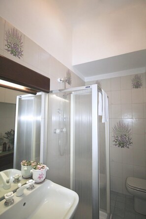 Un baño con ducha de vidrio, un lavamanos blanco con dos llaves y un inodoro.