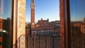 A balcony with a view of a historic building with a clock tower and a square. - Torre del Campo (Siena)