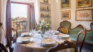 A dining room with a table set for six, a vase of flowers, and a view of a cityscape through an open window. - Torre del Campo (Siena)