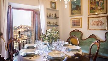 A dining room with a table set for six, a vase of flowers, and a view of a cityscape through an open window.