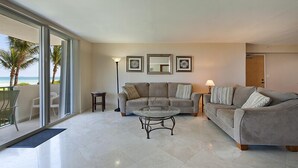 A spacious living room with a large glass door leading to a balcony with a view of the ocean. There is a grey sofa set with a glass coffee table in the center. - Spectacular Oceanfront Views in Miami's Safest Beachfront Community  (Surfside)