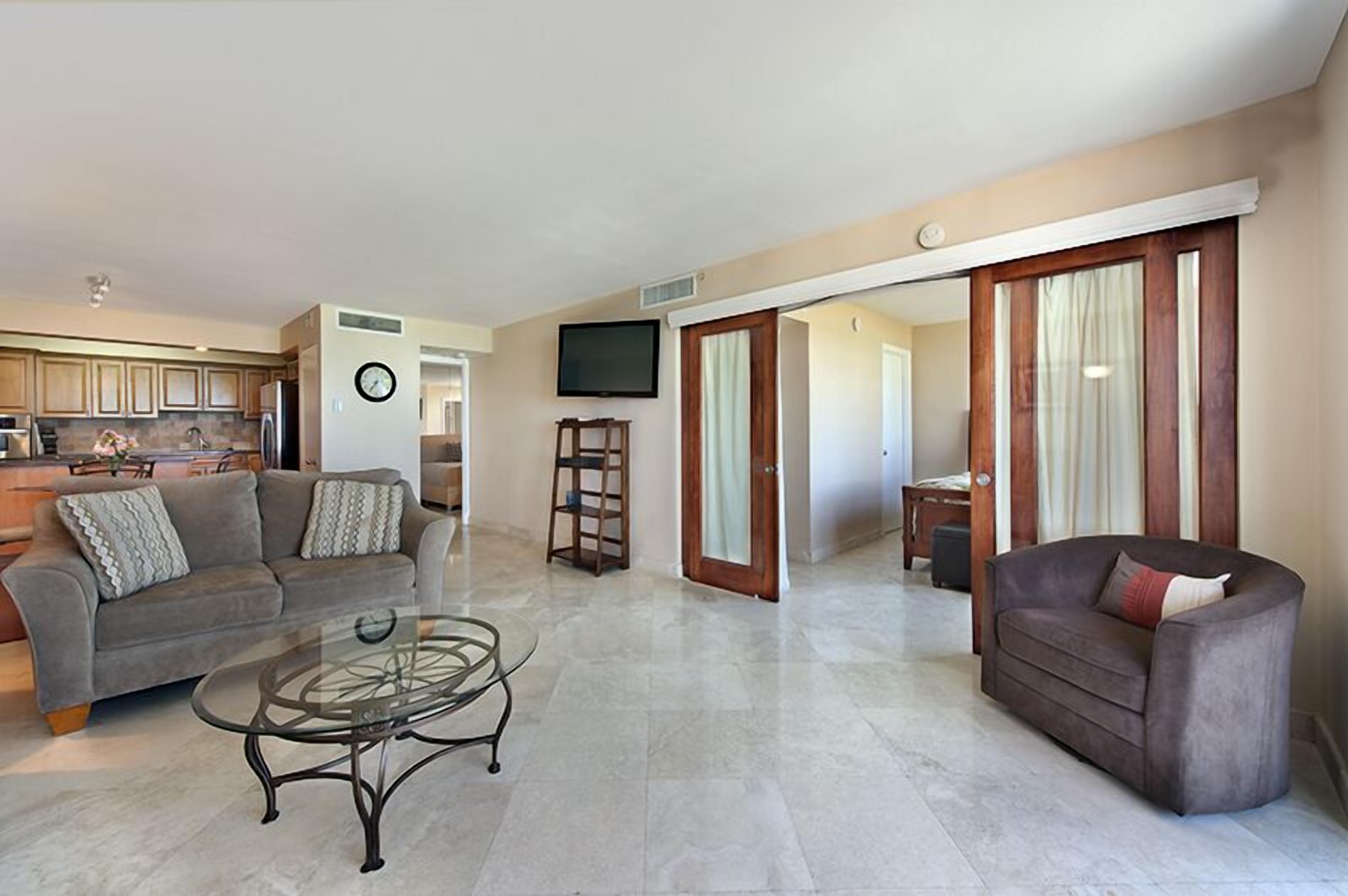 A spacious living area with a sofa, a coffee table, and a television mounted on the wall.