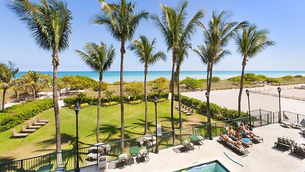 A resort with a pool area, palm trees, and a view of the beach. - Spectacular Oceanfront Views in Miami's Safest Beachfront Community  (Surfside)