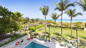 A poolside area with a view of the ocean, palm trees, and a clear sky. - Spectacular Oceanfront Views in Miami's Safest Beachfront Community  (Surfside)