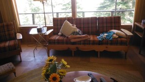 A living room with a plaid sofa, a coffee table with a vase of sunflowers, and a view of trees through large windows. - Mountain Rustic Ski House Tahoe-Reno  Mt Rose-Snow Resort 1.5 Miles (Reno)