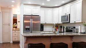 A kitchen with white cabinets, stainless steel appliances, a granite countertop, and three wicker stools.