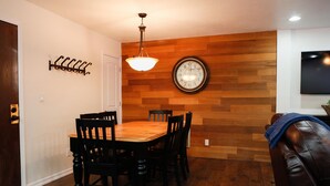 A dining area with a wooden wall, a round clock, and a ceiling light.
