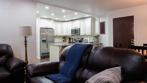 A living room with a brown leather sofa, a lamp, and a kitchen in the background.
