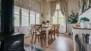 Ein Essbereich mit Holztisch und Stühlen, einem Herd und großen Fenstern mit Vorhängen.