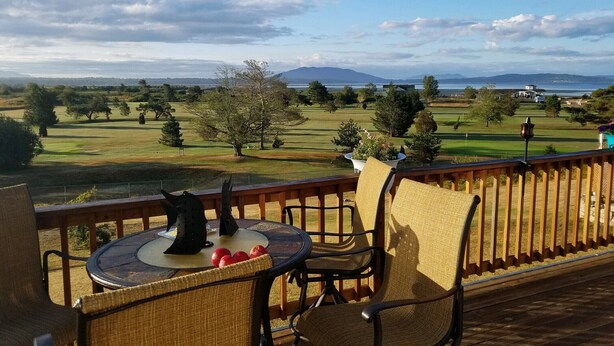 A balcony with wicker chairs and a table, overlooking a golf course and a body of water. - Mt Baker, San Juans, WWU, Sea to Ski race,  Canada, Golf, Refineries, 2 Bd/2 bth (Ferndale)