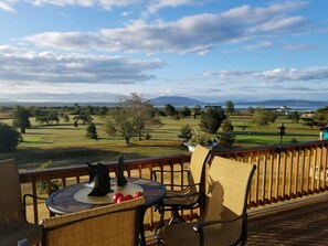 Un balcón con sillas de mimbre y una mesa, con vista a un campo de golf y una masa de agua.