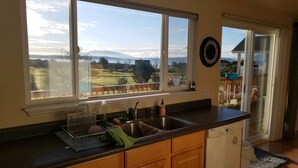 A kitchen with a large window, wooden cabinets, a dishwasher, and a view of a golf course and mountains. - Mt Baker, San Juans, WWU, Sea to Ski race,  Canada, Golf, Refineries, 2 Bd/2 bth (Ferndale)