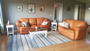 A living room with two brown leather sofas, a white coffee table, and a striped rug. There are framed pictures on the wall and a small white side table with a decorative item. - Mt Baker, San Juans, WWU, Sea to Ski race,  Canada, Golf, Refineries, 2 Bd/2 bth (Ferndale)