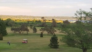 A golf course with a golf cart and a person in the foreground, surrounded by trees and open fields. - Mt Baker, San Juans, WWU, Sea to Ski race,  Canada, Golf, Refineries, 2 Bd/2 bth (Ferndale)