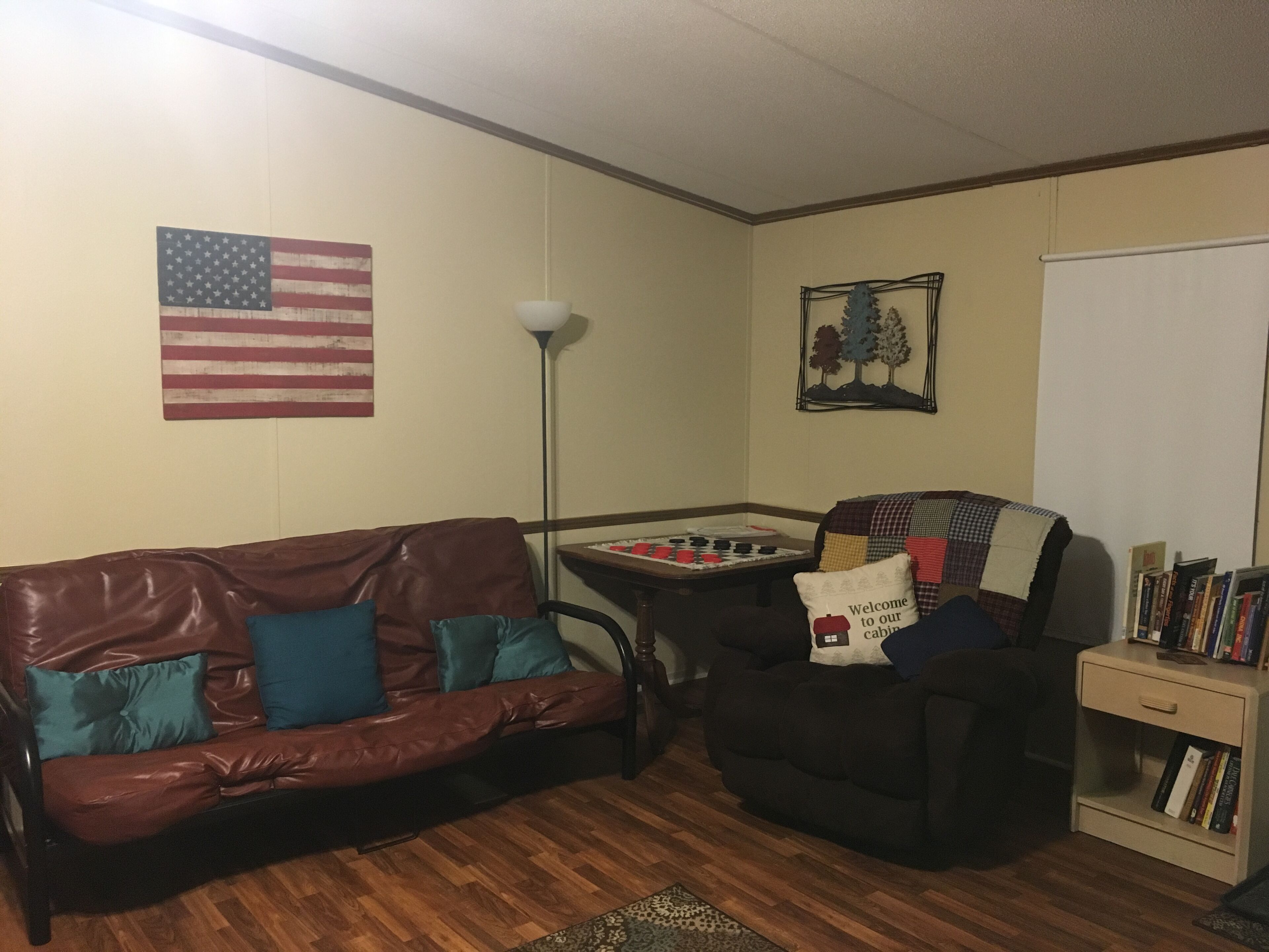 Una sala de estar con un sofá de cuero marrón, un sillón negro, una mesa de fútbol y una estantería.