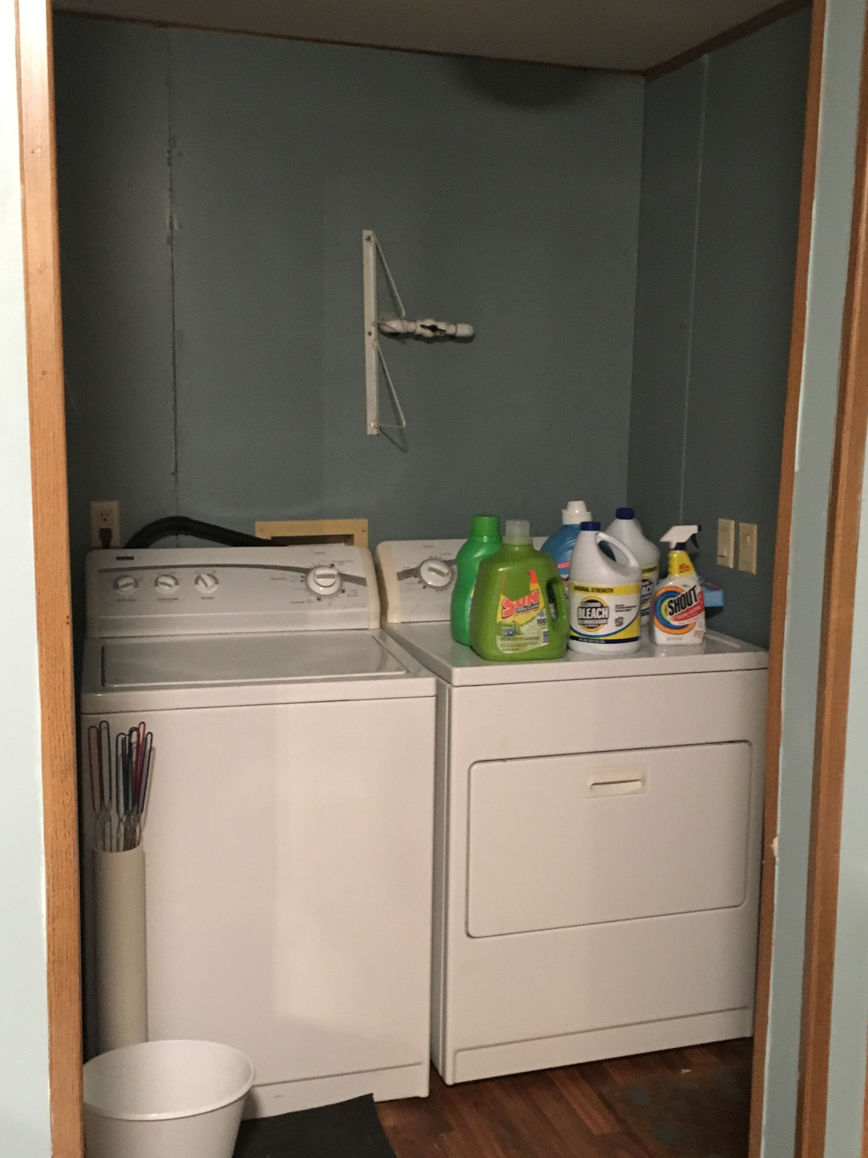 A laundry area with a washing machine and dryer, a metal rack, and cleaning supplies on the dryer.